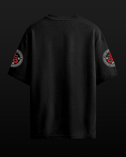 A black t-shirt shown from the back, featuring circular sleeve graphics with red and white text and design elements, set against a dark background.