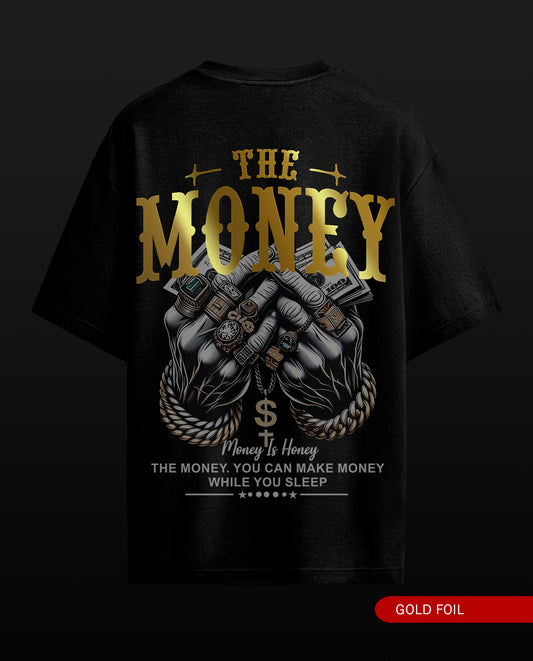 A black short-sleeve graphic T-shirt shown from the back on a dark background. The shirt features a large gold and white print with the words 'THE MONEY' and 'Money Is Honey' above and below an illustration of hands holding cash and wearing watches.