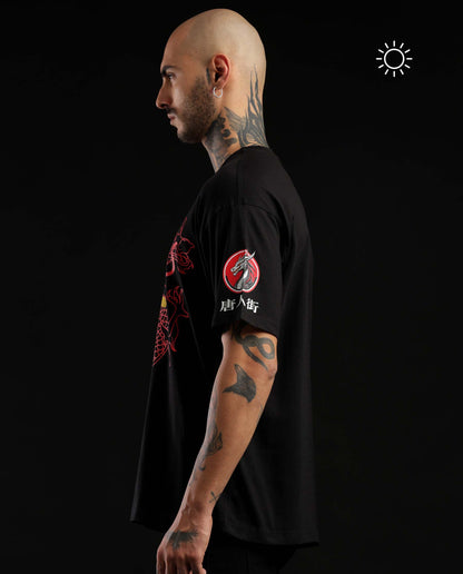 A man in profile wearing a black short-sleeve t-shirt with red and white graphics on the front and sleeve, set against a solid black background.